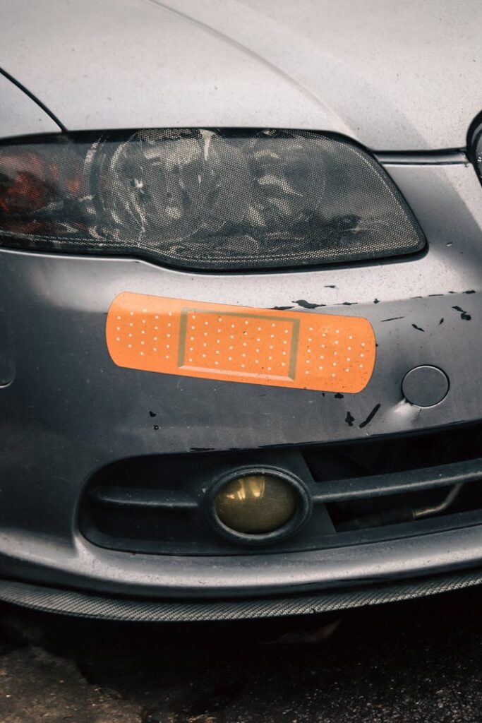 Close-up of a car's headlight with a humorous bandage sticker, suggesting repair.
