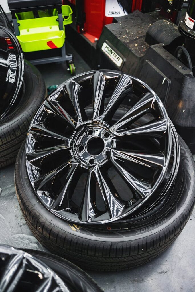 Glossy black car wheel rim and tire stack in an automotive workshop.