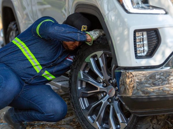 Mechanic working on the wheel of a white off-road vehicle outdoors, fixing a problem.