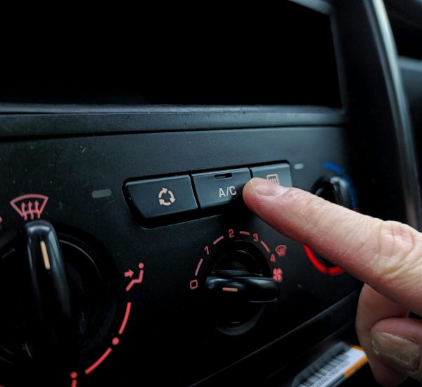 Close-up of a person adjusting a car's air conditioning system inside a vehicle cabin.