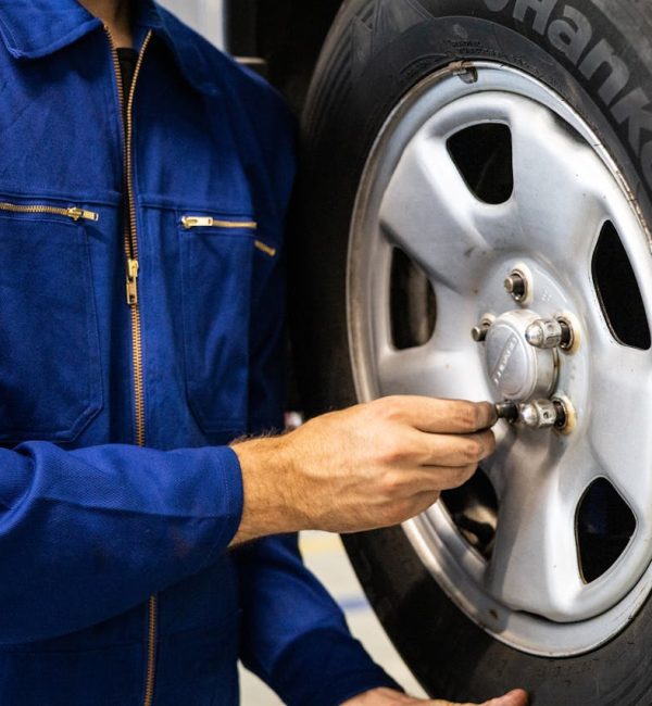 Mechanic in blue coveralls inspecting a car tire in an auto repair workshop.